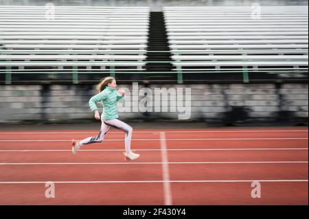 Side View of Determined Young Athletic Girl Running on Red Track Stock Photo