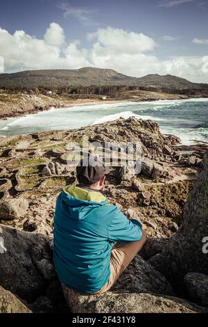 Man in blue jacket and black cap looking at the sea Stock Photo