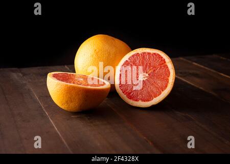 half cut ripe grapefruit and whole grapefruit on brown rustic wooden table with black background Stock Photo