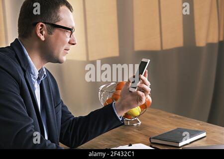 Young businessman wearing suit and glasses looking at his mobile phone while sitting at a table Stock Photo