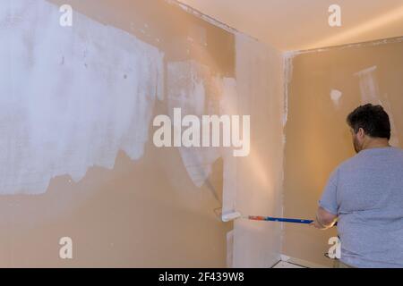 Long handle roller brush applying white primer paint on wall with home renovation Stock Photo