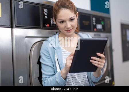 young woman using digital tablet while sitting against washing machines Stock Photo