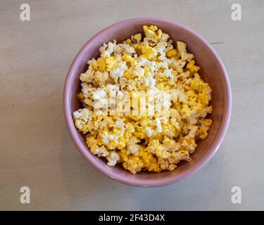 Popcorn, or popped corn, in a pink bowl on a table. Stock Photo