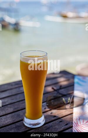 Mango juice on the beach with the sea on the background. Sanur, Bali, Indonesia. Vertical image. Stock Photo