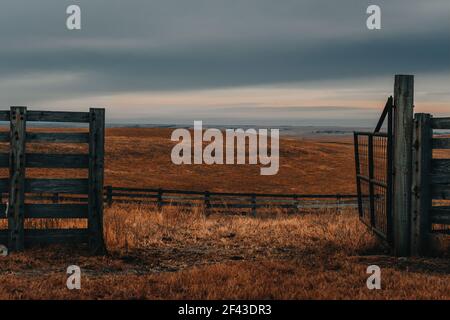 Open gate looking out onto the rolling hills of long grass prairie in Kansas under dramatic lighting Stock Photo