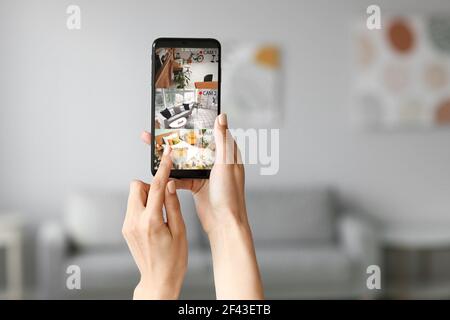 Woman with mobile phone looking at the images of cctv cameras installed in apartment Stock Photo