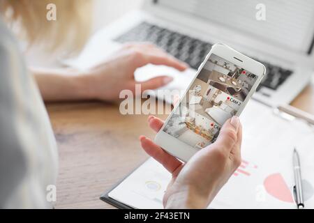 Woman with mobile phone looking at the images of cctv cameras installed in apartment Stock Photo