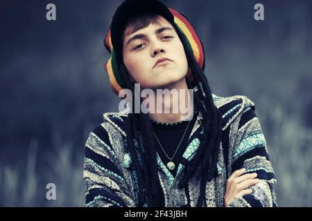 Sad young fashion hipster man walking outdoor Stylish trendy model in rasta hat and poncho Stock Photo