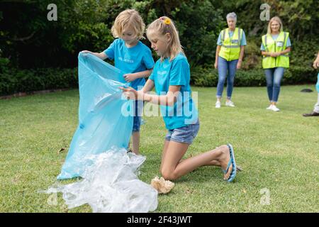 Caucasian boy and girl with volunteer group kneeling collecting plastic rubbish in field Stock Photo