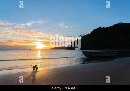 Anchor and chain to dinghy in silhouette at waters edge Mulberry Grove Beach Great Barrier Island New Zealand. Stock Photo
