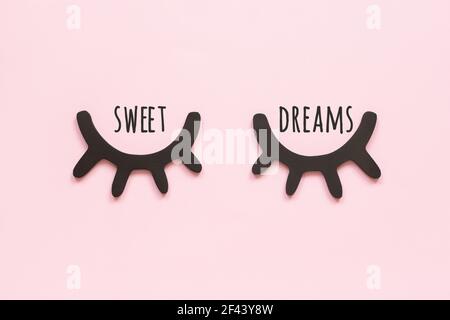 Sweet dreams text and decorative black wooden eyelashes, closed eyes on pink background. Concept Good night. Top view Copy space. Stock Photo