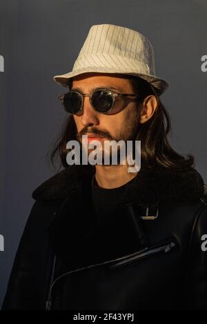 Portrait of a young man wearing sunglasses, white hat and black leather jacket. Stock Photo