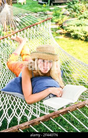A woman reading a book while relaxing on a hammock outdoors. Stock Photo