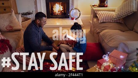Stay safe text over father with daughter opening present at christmas Stock Photo