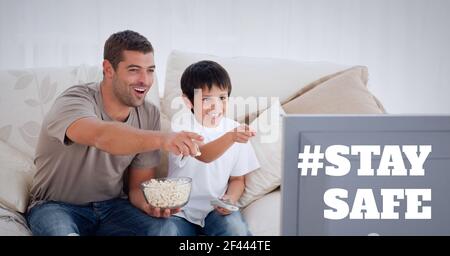 Stay safe text over father and son watching television and eating popcorn Stock Photo