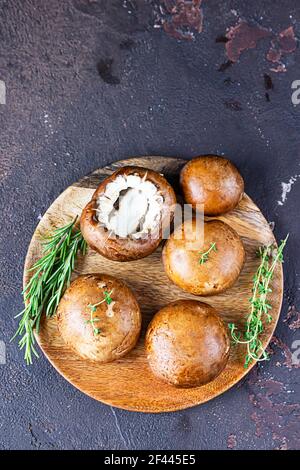 Fresh delicious portobello mushrooms with thyme and rosemary on wooden cutting board, dark stone background. Stock Photo