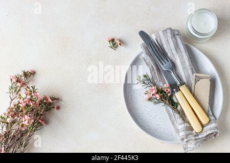 Romantic or spring table setting. Knife and fork, little pink flowers and linen napkin on a plate, light concrete background. Flat lay. Selective focu Stock Photo