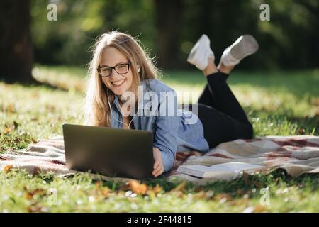 Woman lying at park and surfing internet on laptop Stock Photo