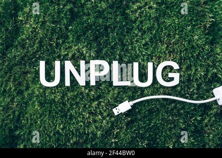 Word Unplug, white internet usb adapter on moss, green grass background. Top view. Copy space. Banner. Biophilia concept. Nature backdrop Stock Photo