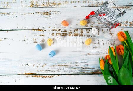 Multicolor Easter painted speckled eggs in basket on white wooden table with tulips. Traditional Spring composition Easter elements flowers and eggs for springtime. Spring decorations concept Stock Photo