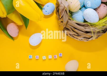 Easter holiday decorations on yellow background Colorful easter painted speckled eggs in basket. Traditional Spring composition Easter elements flowers and eggs for springtime easter greeting card Stock Photo