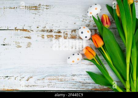 Multicolor Easter painted speckled eggs in basket on white wooden table with tulips. Traditional Spring composition Easter elements flowers and eggs for springtime. Spring decorations concept Stock Photo