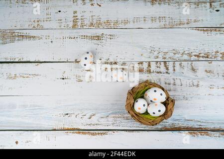 Multicolor Easter painted speckled eggs in basket on white wooden table with tulips. Traditional Spring composition Easter elements flowers and eggs for springtime. Spring decorations concept Stock Photo