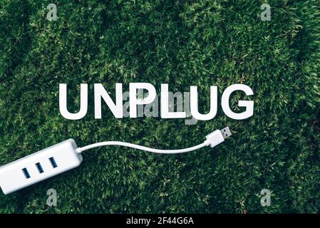 Word Unplug, white internet usb adapter on moss, green grass background. Top view. Copy space. Banner. Biophilia concept. Nature backdrop Stock Photo