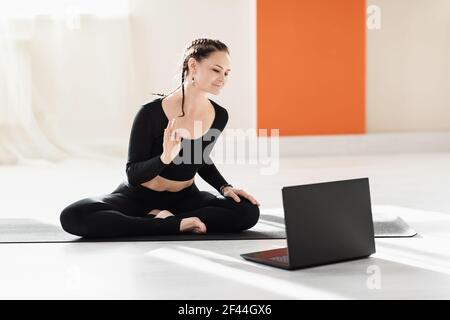 Woman universal yoga trainer greets pupils at the laptop before doing an online workout. Stock Photo