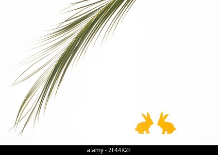 Palm Sunday concept. Palm tree branch and yellow bunnies on white background. Minimal design. Copy space. Stock Photo