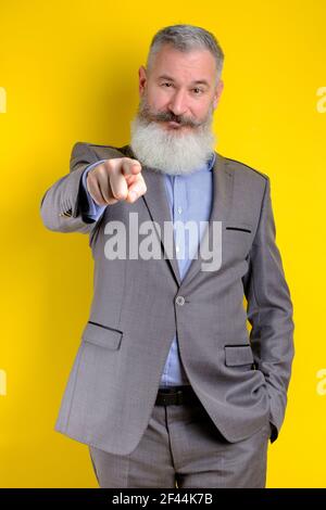 Studio portrait mature businessman dressed in gray suit points on camera, I choose you concept, yellow background Stock Photo