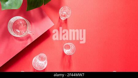 Glasses of water top view summer composition on bright red background. Still life with monstera palm leaf and long shadows, with copy space Stock Photo