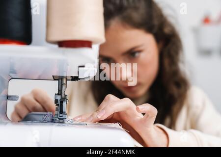 Serious charming girl seamstress working with sewing machine in atelier Stock Photo