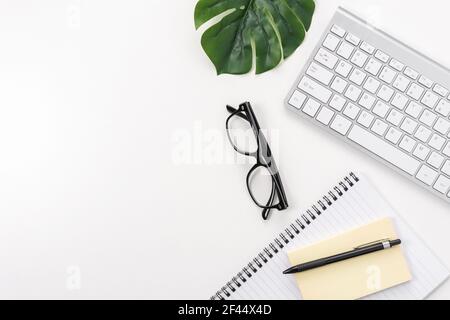 White office desk table with blank notebook, computer keyboard and other office supplies. Top view with copy space. Stock Photo