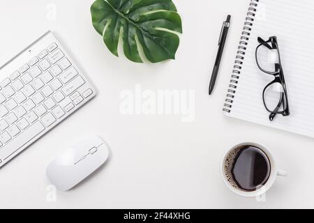 Workspace with computer keyboard, office supplies, green leaf, and coffee cup on white background. Stock Photo