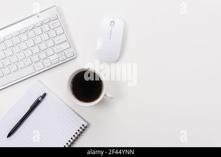 White office desk table with blank notebook, computer keyboard and other office supplies. Top view with copy space. Stock Photo