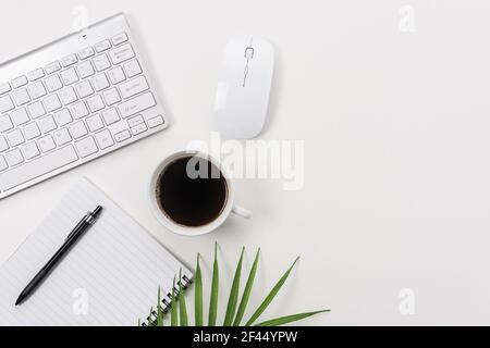 Workspace with computer keyboard, office supplies, green leaf, and coffee cup on white background. Stock Photo