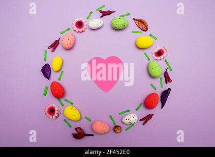 Easter layout made of colorful eggs and flowers on purple background with pink heart in the middle. Spring holidays concept, flat lay Stock Photo