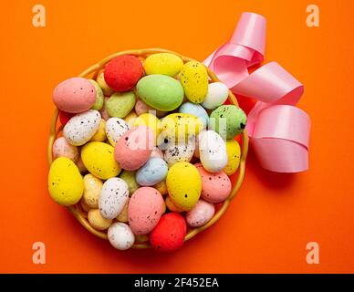 Colorful Easter eggs in the basket with pink ribbon on orange background. Spring holidays concept Stock Photo