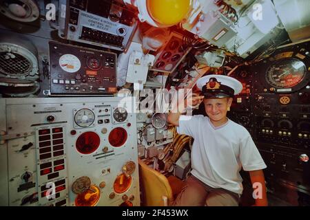 Young boy wearing a Navy officer peak cap saluting from the Helm of the Pilot's station onboard Oberon class submarine HMS Ocelot. HM Submarine Ocelot. Chatham historic dockyard. Kent. England. UK Stock Photo