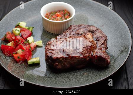 Meat steak with vegetables and sauce, on a light plate, on a black background Stock Photo