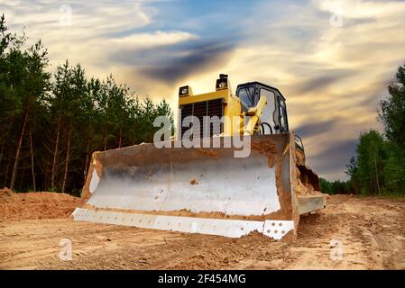 Dozer during clearing forest for construction new road. Bulldozer at forestry work on sunset background. Earth-moving equipment at road work, land cle Stock Photo