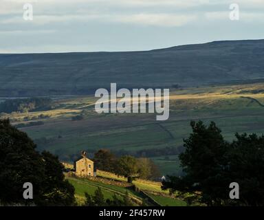 A lone house in sunlight against a backdrop of dark, brooding hills (Weardale, the North Pennines, County Durham, UK) Stock Photo