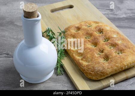Rosemary focaccia over wood board with ceramic olive oil bottle. Stock Photo