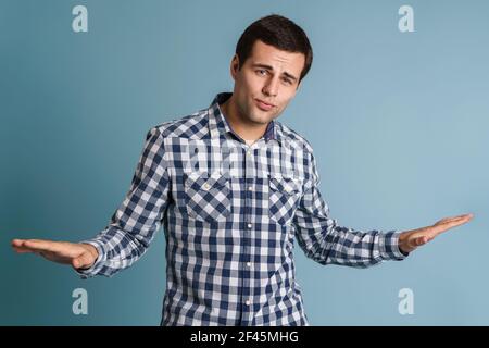 Confused young man doubting and shrugging shoulders in questioning gesture isolated over blue background Stock Photo