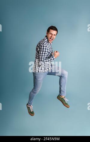 Happy young casual man jumping isolated over blue background, celebrating, full length Stock Photo