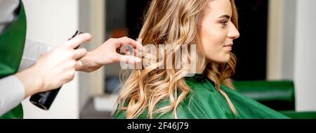 Side view of female hairdresser using hairspray fixing client's female hair in a hair salon Stock Photo