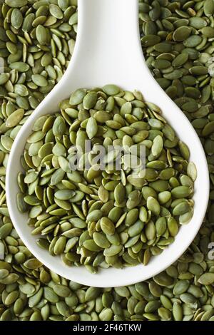 Pumpkin seeds on and beside white spoon Stock Photo