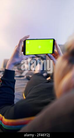 Young blond woman relaxing on the couch and using smartphone with green screen. High quality photo Stock Photo