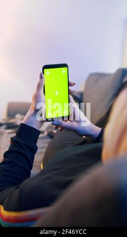 Green screen on the smartphone in the hands of young woman relaxing on the couch. High quality photo Stock Photo